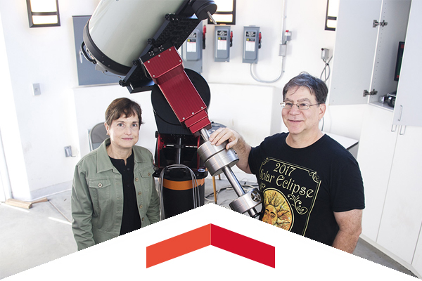 Professors Cristina Cadavid and Damian Christian pose with a large telescope. 