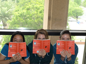 Three students hiding behind "The Curious Incident of the Dog in the Night-time"