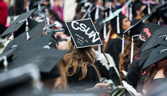 commencement scene with graduate wearing mortarboard that has "dreams do come true" written on it.