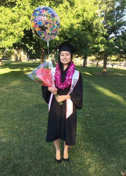 Julie at graduation with CSUN sash and flower lei holding graduation bouquet and balloon 