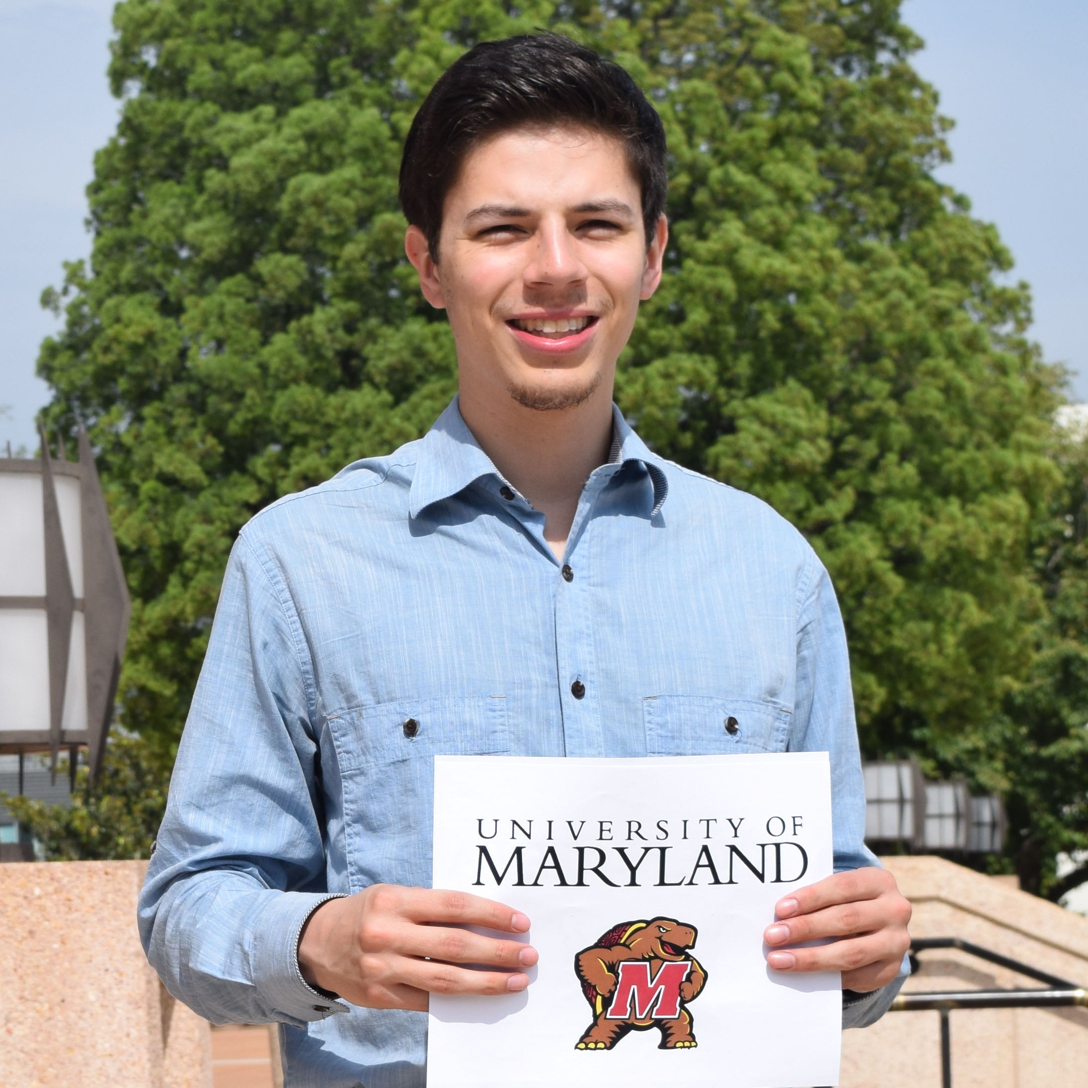Richard holds sign with showing his graduate school of choice, the University of Maryland