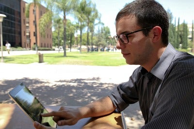 A male CSUN student using a tablet outdoors on campus.