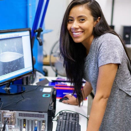 Female student smiling in front of lab equipment.