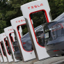 Two gray cars parked at a row of Tesla electric vehicle charging stations.